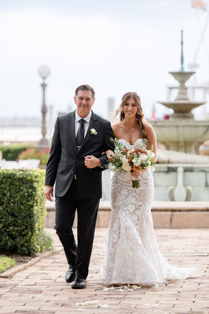 bride and her father walk down the aisle during an outdoor wedding ceremony at Epping Forest Yacht Club in Jacksonville, Florida, captured by Snapshots by Gabriela