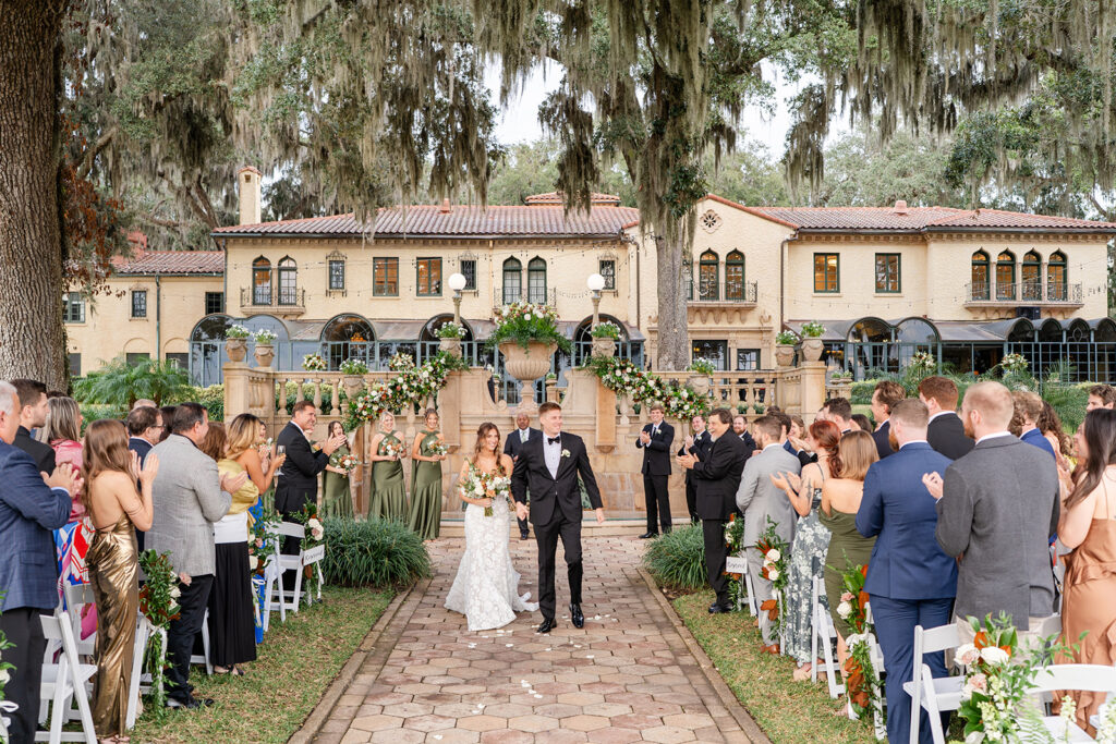 bride and groom walk down an outdoor brick aisle surrounded by cheering guests at a wedding at Epping Forest Yacht Club in Jacksonville, Florida, captured by Snapshots by Gabriela