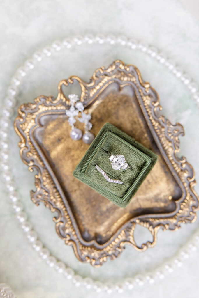 wedding details shots with ornate gold tray holding with a mossy green velvet ring box with an oval diamond ring and earrings