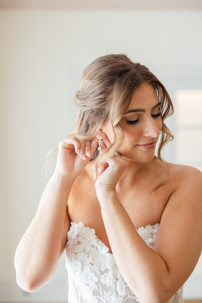 a bride putting on her earring while getting ready for her wedding at Epping Forest Yacht Club in Jacksonville, Florida, captured by Snapshots by Gabriela