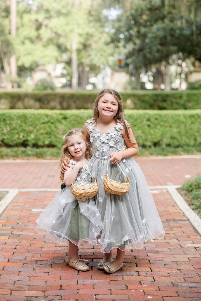 two flower girls wearing sage green floral dresses carrying wicker baskets at Epping Forest Yacht Club in Jacksonville, Florida, captured by Snapshots by Gabriela