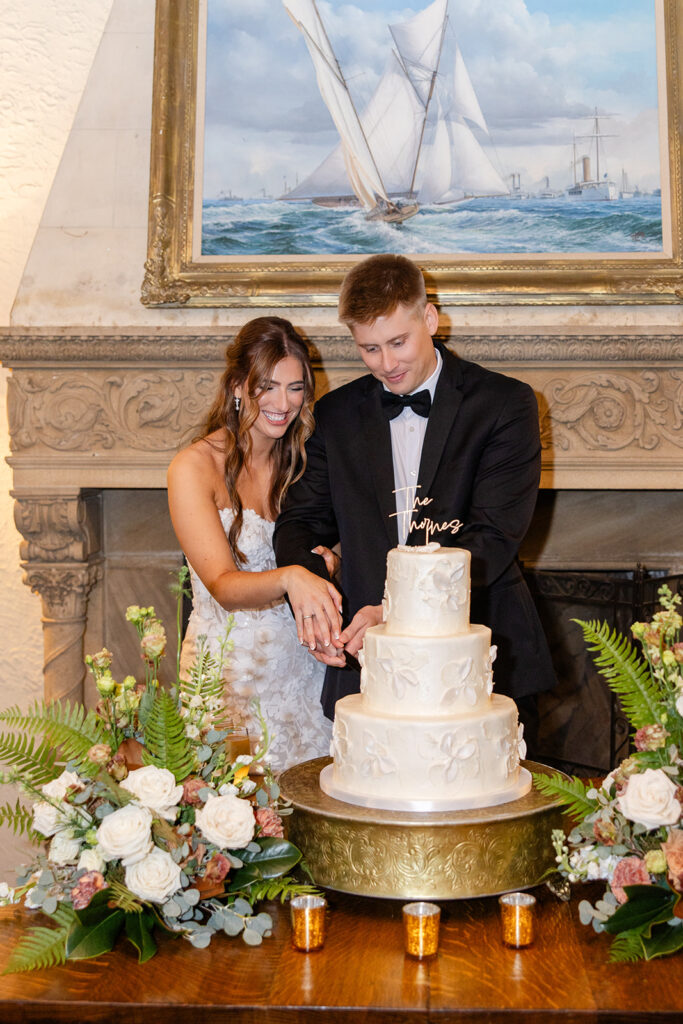bride and groom cutting their cake in front of a sailboat painting at Epping Forest Yacht Club in Jacksonville, Florida, captured by Snapshots by Gabriela