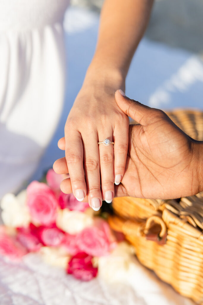 woman's hand wearing an engagement ring over a picnic setup in a beach engagement photo at Jetty Park Beach in Cape Canaveral, Florida, captured by Snapshots by Gabriela
