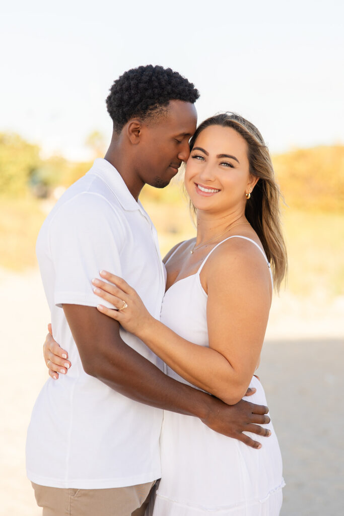 couple wearing white embrace in a beach engagement photo at Jetty Park Beach in Cape Canaveral, Florida, captured by Snapshots by Gabriela