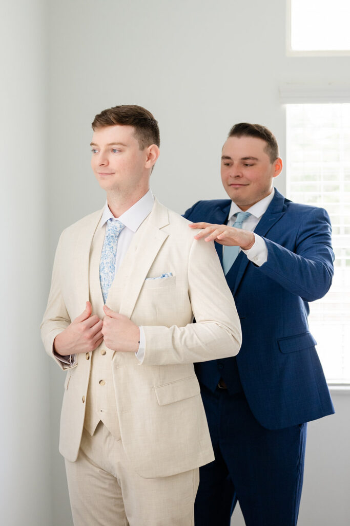 groom in a tan linen suit getting dressed with a groomsman at a wedding at Bella Cosa Lakeside in Lake Wales Florida