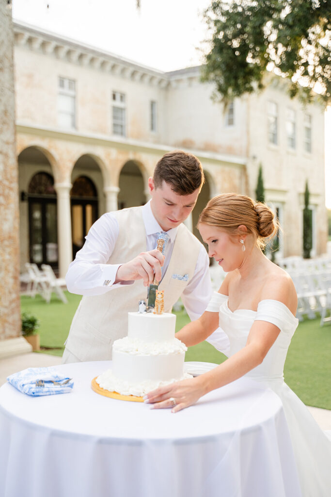 bride and groom cut their white wedding cake with cat cake topper at a wedding reception at Bella Cosa Lakeside in Lake Wales Florida