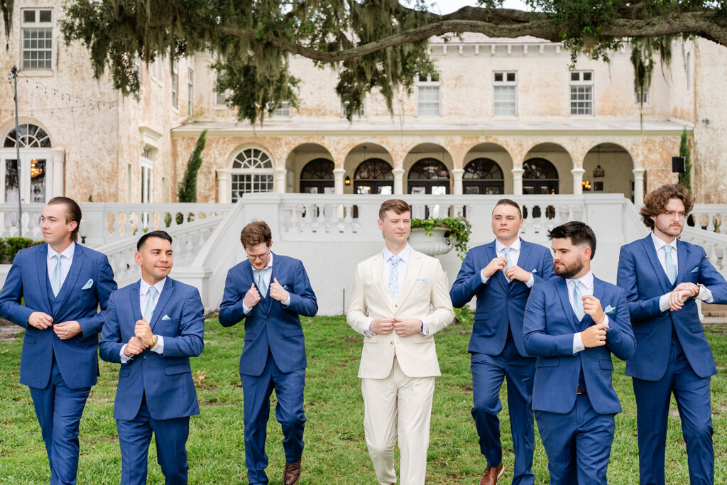 groom in tan linen suit walking on the lawn with groomsmen in blue suits at a wedding at Bella Cosa Lakeside in Lake Wales Florida