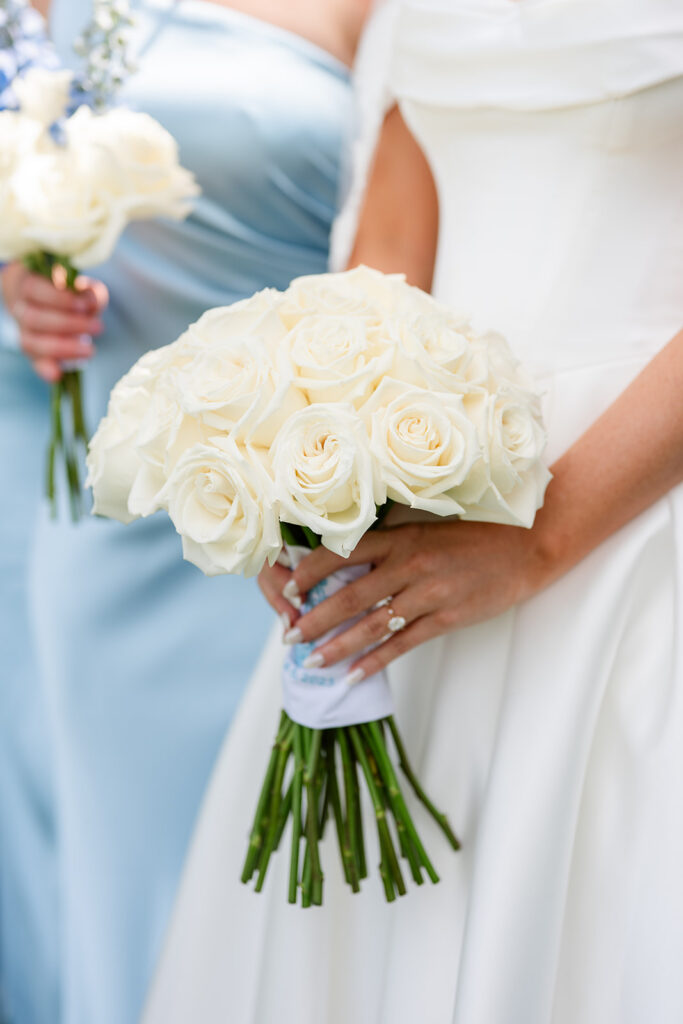 bride's hand holding a bouqet of white roses tied with a blue satin ribbon at a wedding at Bella Cosa Lakeside in Lake Wales Florida