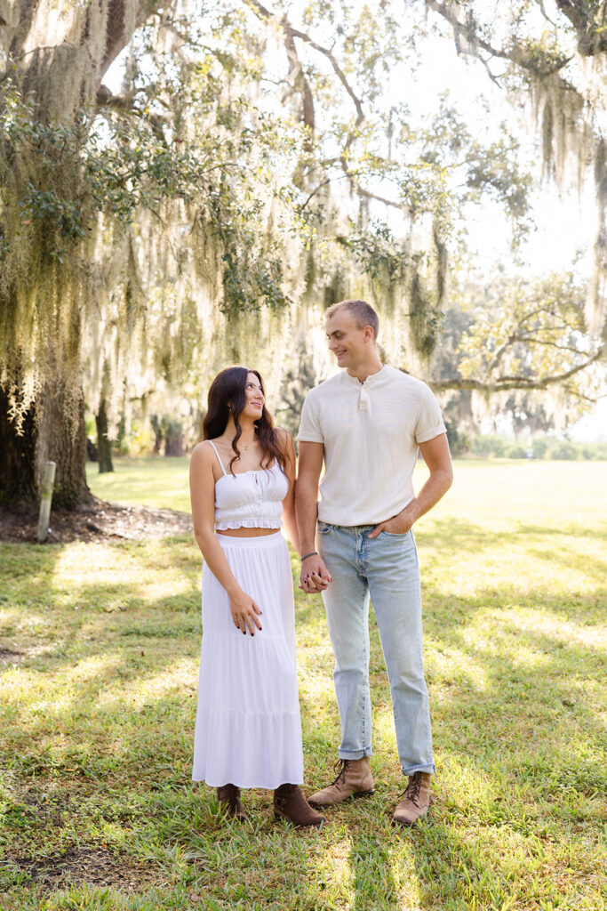 Couple poses naturally in front of trees in a casual engagement photo at Bok Tower Gardens captured by Snapshots by Gabriela.