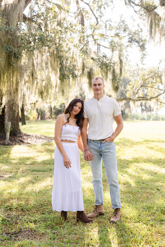 Couple poses naturally in front of trees in a casual engagement photo at Bok Tower Gardens captured by Snapshots by Gabriela.