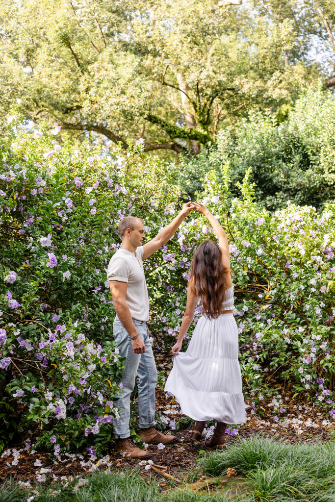 couple twirls in front of purple flowers in a casual engagement photo at Bok Tower Gardens captured by Snapshots by Gabriela.