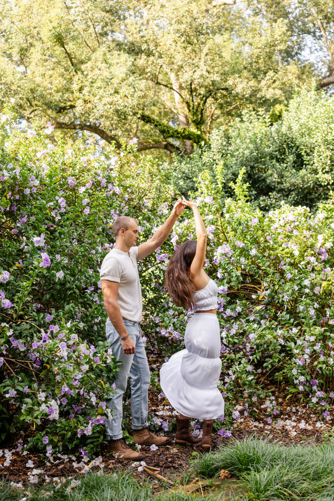 couple twirls in front of purple flowers in a casual engagement photo at Bok Tower Gardens captured by Snapshots by Gabriela.