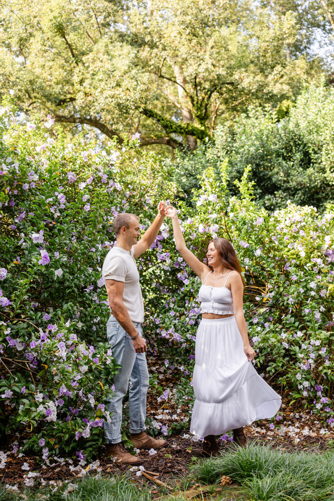 couple twirls in front of purple flowers in a casual engagement photo at Bok Tower Gardens captured by Snapshots by Gabriela.
