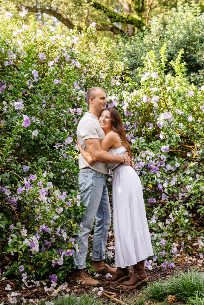 couple embraces in front of purple flowers in a casual engagement photo at Bok Tower Gardens captured by Snapshots by Gabriela.