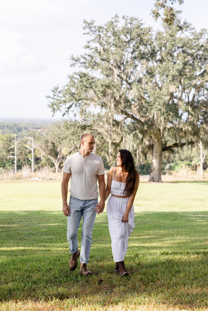 couple walks on a grassy lawn in a casual engagement photo at Bok Tower Gardens captured by Snapshots by Gabriela.