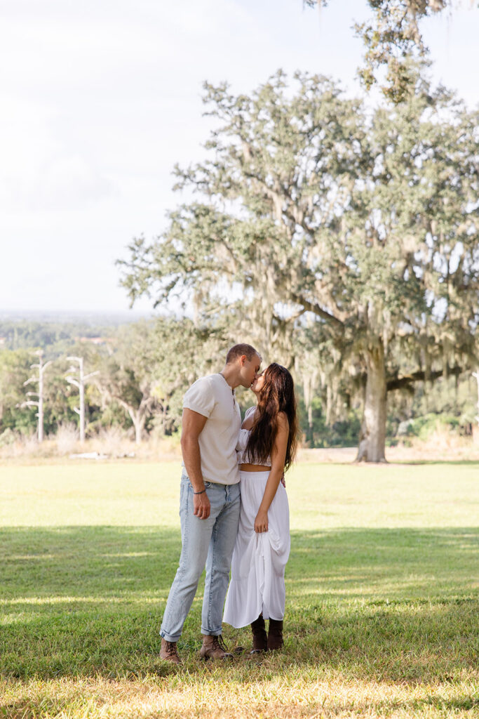 couple kisses on a grassy lawn in a casual engagement photo at Bok Tower Gardens captured by Snapshots by Gabriela.