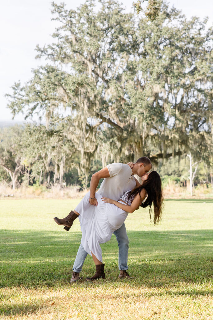 couple dips while kissing on a grassy lawn in a casual engagement photo at Bok Tower Gardens captured by Snapshots by Gabriela.