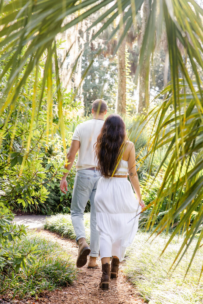 couple walks down a nature path in a casual engagement photo at Bok Tower Gardens captured by Snapshots by Gabriela.