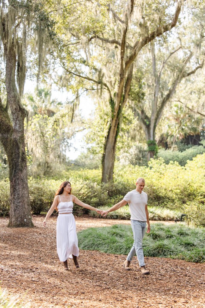 couple walks down a nature path in a casual engagement photo at Bok Tower Gardens captured by Snapshots by Gabriela.