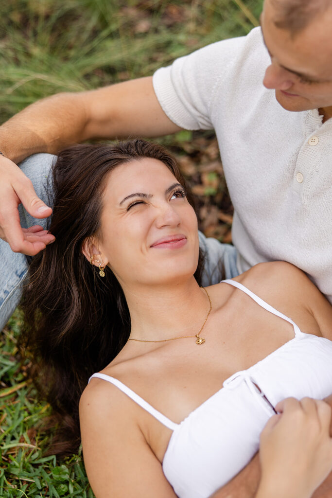 couple embraces on the ground on a grassy lawn in a casual engagement photo at Bok Tower Gardens captured by Snapshots by Gabriela.
