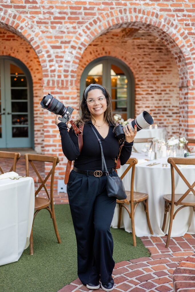 a behind-the-scenes photo of Gabriela from Snapshots by Gabriela, an Orlando wedding photographer, holding two cameras at a wedding venue