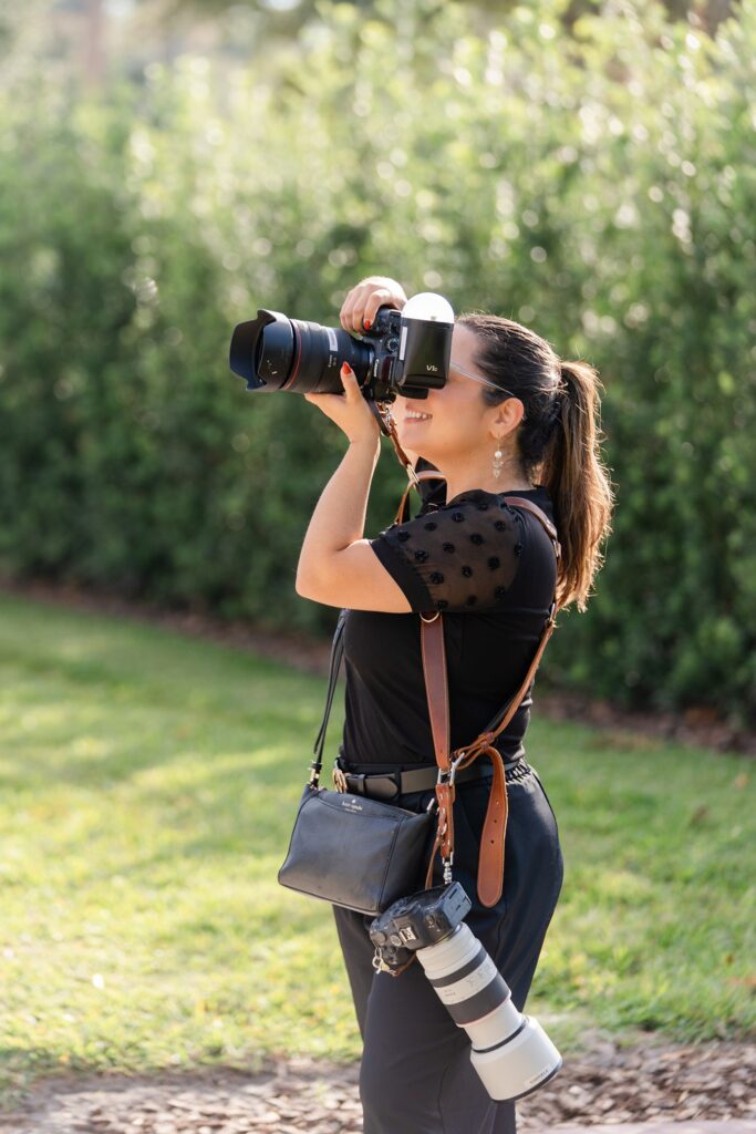 a behind-the-scenes photo of Gabriela from Snapshots by Gabriela, an Orlando wedding photographer, taking a photo on a wedding day with all of her gear