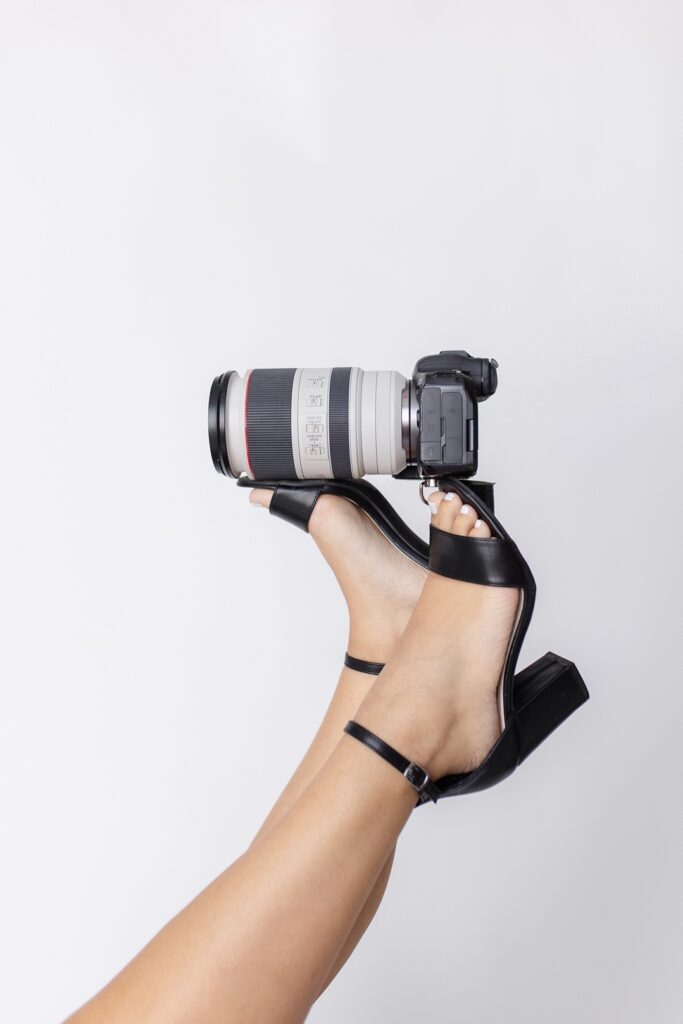 a branding photo of Gabriela from Snapshots by Gabriela, an Orlando wedding photographer, posing with her feet balancing her camera 
