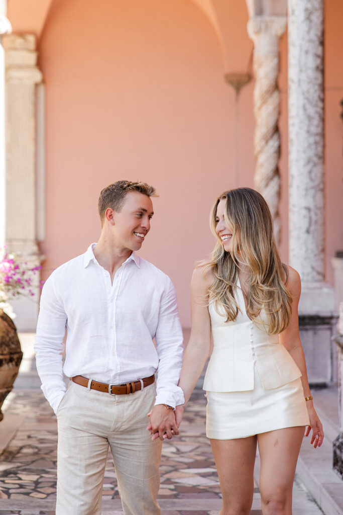 Woman in white mini-dress and man in white shirt and khaki pants under pink archways at The Ringling Museum in Sarasota for their engagement photos captured by Snapshots by Gabriela