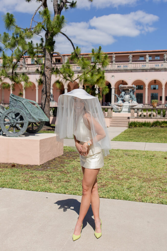 Woman in white mini-dress and hat with bridal veil at The Ringling Museum in Sarasota for their engagement photos captured by Snapshots by Gabriela