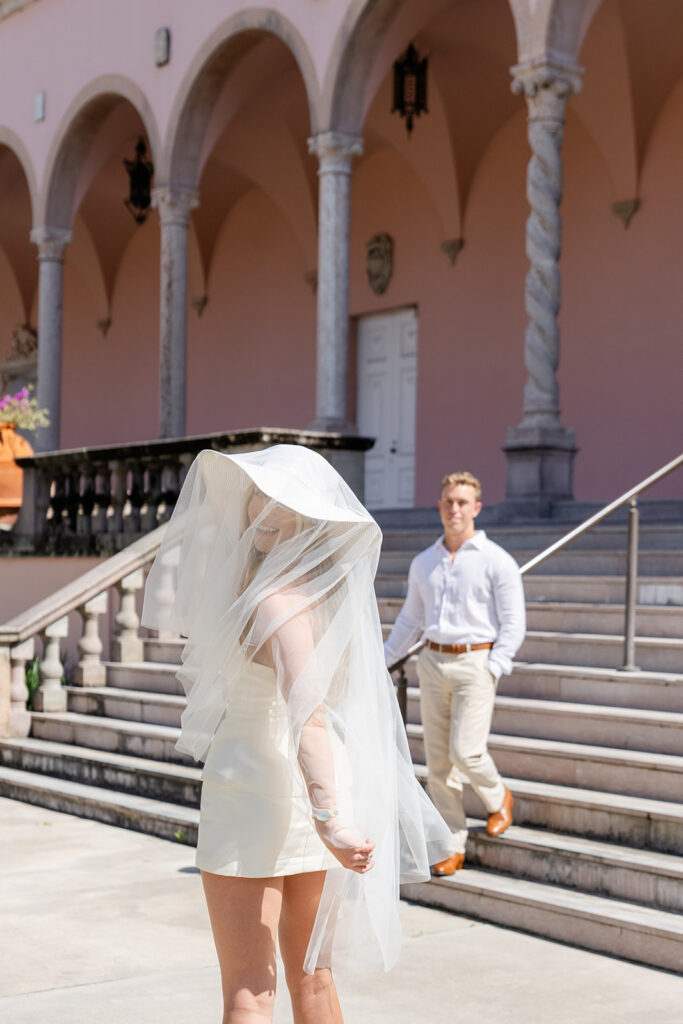 Woman in white mini-dress and hat with bridal veil at The Ringling Museum in Sarasota for their engagement photos captured by Snapshots by Gabriela