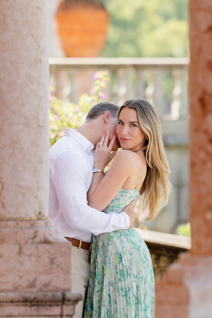Woman in green floral dress and man in white shirt and khaki pants under pink archways at The Ringling Museum in Sarasota for their engagement photos captured by Snapshots by Gabriela
