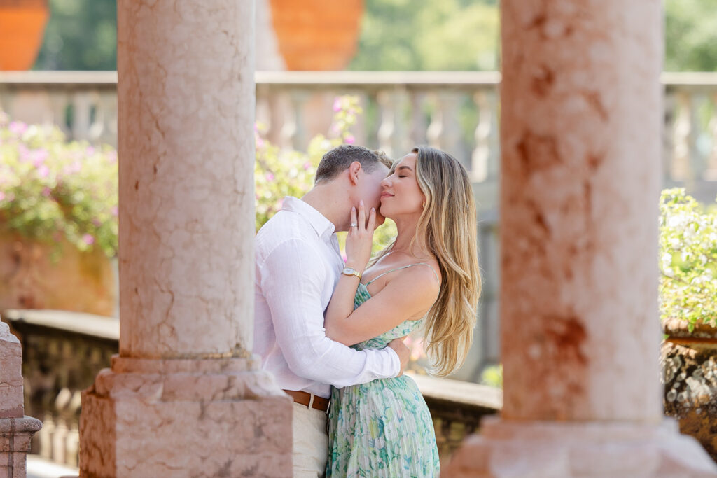 Woman in green floral dress and man in white shirt and khaki pants under pink archways at The Ringling Museum in Sarasota for their engagement photos captured by Snapshots by Gabriela