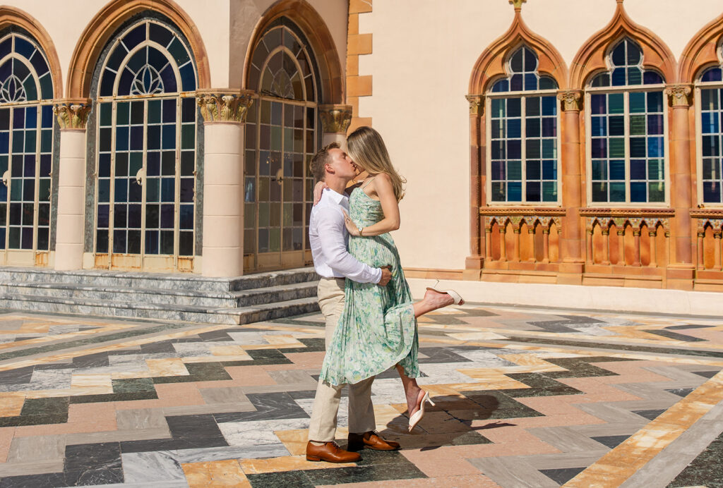 Woman in green floral dress and man in white shirt and khaki pants on the bayside terrace with marble chevrons at The Ringling Museum in Sarasota for their engagement photos captured by Snapshots by Gabriela