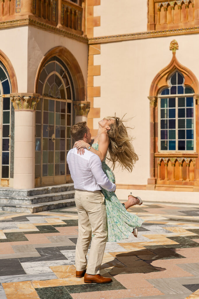 Woman in green floral dress and man in white shirt and khaki pants on the bayside terrace with marble chevrons at The Ringling Museum in Sarasota for their engagement photos captured by Snapshots by Gabriela