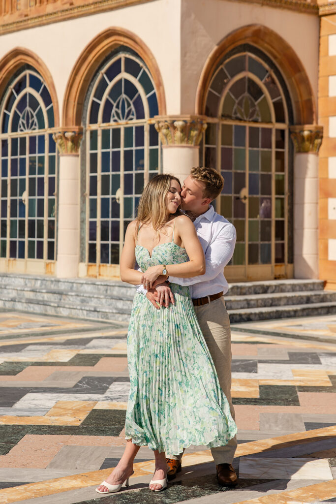 Woman in green floral dress and man in white shirt and khaki pants on the bayside terrace with marble chevrons at The Ringling Museum in Sarasota for their engagement photos captured by Snapshots by Gabriela